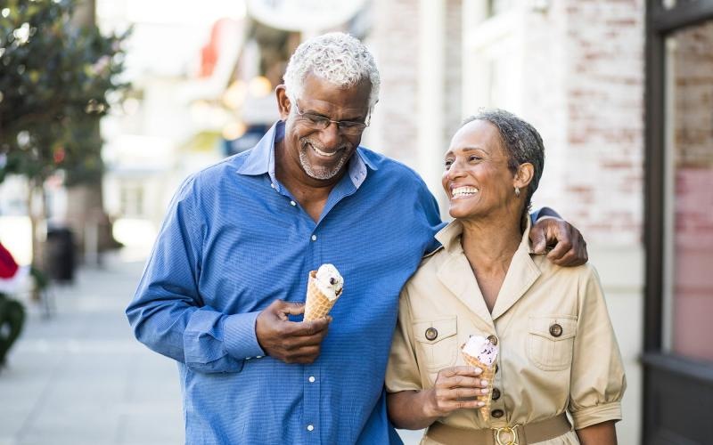 older couple walks down city sidewalk while holding ice cream cones